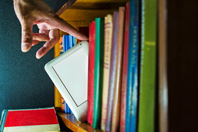 Image of a man pulling an ereader off of a bookshelf
